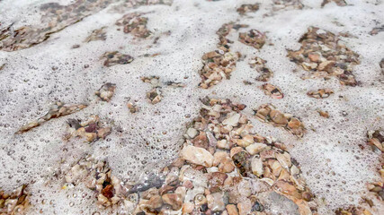 Waves gently wash over a pebbled beach, creating a serene natural texture ideal for environmental concepts or summer relaxation
