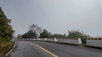 Fototapeta premium Empty mountain road with protective barriers and lush greenery under a cloudy sky, representing travel and adventure in nature