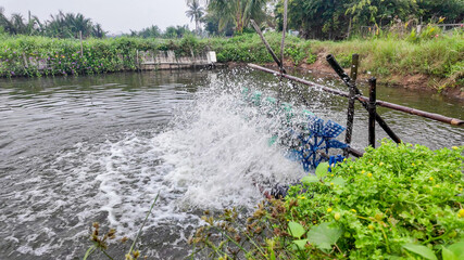 A paddle wheel aerator splashes vigorously in a lush green canal, illustrating sustainable aquaculture and water oxygenation techniques