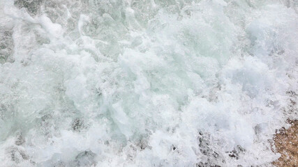 Waves crash onto the shore creating frothy sea foam, symbolizing nature's power and coastal erosion awareness