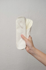 A woman's hand holding a sanitary pad on a gray background. Hygienic concept © Lys Owl