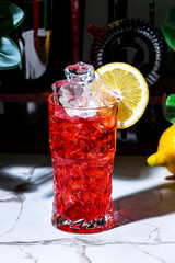 Bitter lemon cooler alcoholic cocktail drink with gin, dry vermouth, juice, grenadine, soda, ice and lemon. Marble table in lounge bar with green plants