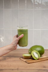 A woman's hand holds a glass glass with a healthy green smoothie with fresh kiwi and celery