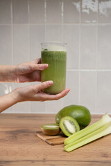 A woman's hand holds a glass glass with a healthy green smoothie with fresh kiwi and celery