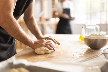 Closeup of baker hands kneading raw dough on kitchen table in bakery
