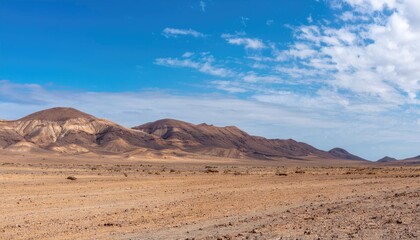 Fototapeta premium Vast desert landscape with mountains under a bright blue sky and scattered clouds. Nature and wilderness concept
