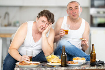 Two adult men drinking beer and watching TV