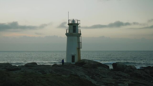 Persona andando al lado de un faro cerca del mar con cielo nublado