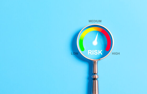 Business Risk Assessment and Management Concept. A magnifying glass highlighting a risk level gauge on a blue background, indicating low, medium, and high risk for business assessment purposes.