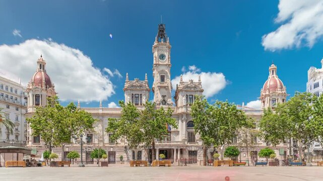 Valencia City Hall (Ajuntament de Valencia) timelapse hyperlapse in Plaza de Ayuntamiento. Historic building with clock tower under a blue cloudy sky. People strolling the main square in Spain