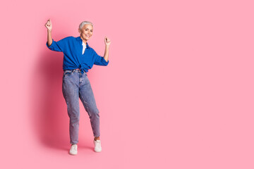 Full length photo of adorable good mood woman wear blue shirt dancing empty space isolated pink...
