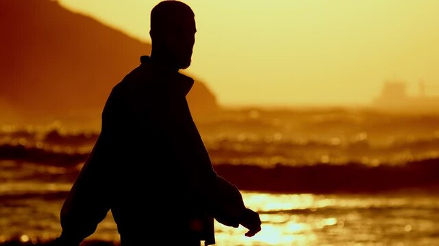 Silueta de hombre andando hacia el mar en el atardecer
