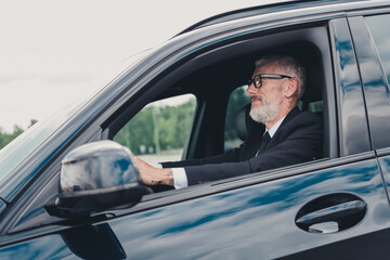 Senior businessman in formalwear driving a car, symbolizing travel and independence on a city street