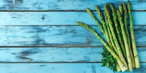 Fresh green asparagus arranged in a minimalistic top view on a weathered blue wooden background with vibrant green parsley accents.
