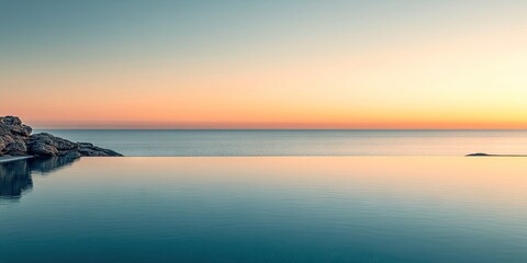 Obraz premium Calm ocean pool reflecting pastel dawn colors with gentle waves at horizon tranquil rocks on the left serene landscape copy space above water