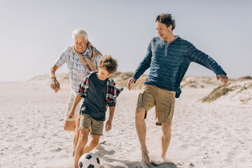 Three generations of men playing soccer on the beach