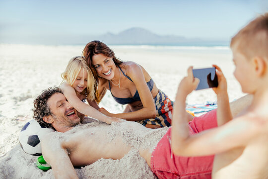 Family having fun burying dad in sand at the beach