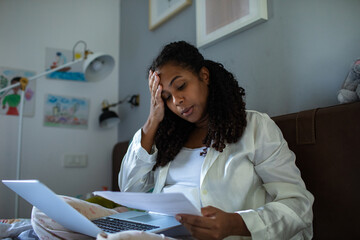 Stressed woman reading documents while working on laptop at home