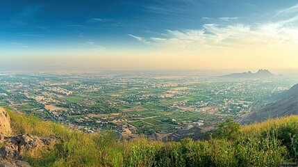 Panoramic sunset view of sprawling city and agricultural landscape from a mountaintop.