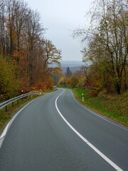 Fototapeta premium Landstraße im Herbst mit Kurvenverlauf durch bewaldete Hügellandschaft