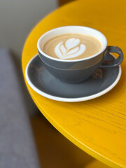 Latte art coffee in grey cup sitting on yellow table