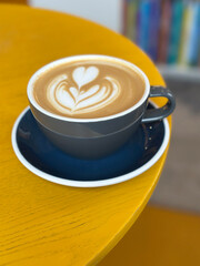 Latte art coffee in gray cup sitting on yellow table in cafe