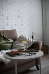  A cozy evening in living room with scene of white wine, candle, notebooks and glasses on white coffee table.
