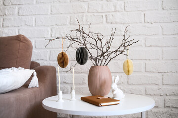 A beautifully cozy living room with modern easter home decor that includes vase with dry branches and eggs, notebook, ceramic rabbit, candles on coffee table.