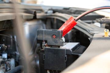 Action of a technician hand is using an emergency clamping kit to clamp on positive polar for jumping the 12V car battery. Transportation troubleshooting and reparing scene, close-up.