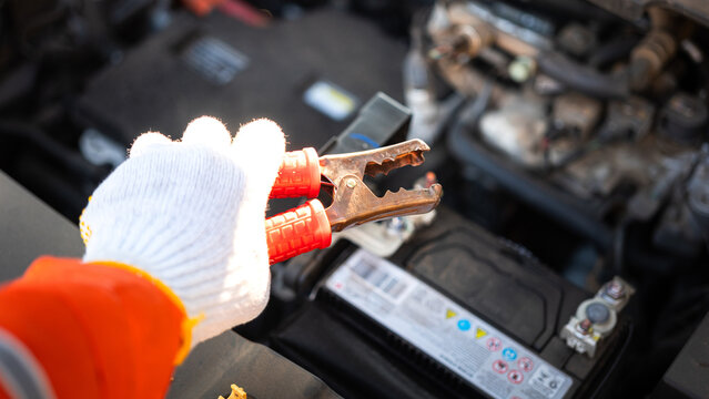 Action of a technician hand is using an emergency clamping kit to clamp on positive polar for jumping the 12V car battery. Transportation troubleshooting and reparing scene, close-up.