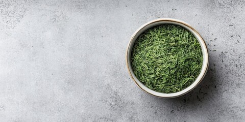 Dried dill leaves in a white bowl centered on a light grey textured surface with ample room for text on the left side of the image