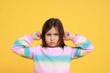 Annoyed little girl covering her ears from loud sound on yellow background