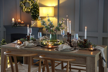 Christmas table setting with stylish dishware, glasses and burning candles in festive decorated room