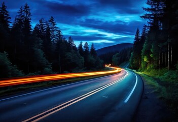 There is a winding road that passes through a dense forest at night