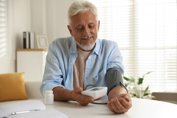 Senior man measuring blood pressure at table indoors