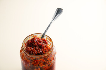 A spoonful of Indonesian spicy sambal resting on top of its glass jar, isolated on a white background