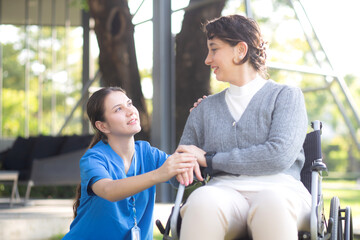 Young caucasian nurse comforting with patient while sitting on wheelchair in outdoor park, doctor...
