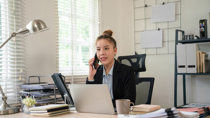 Businesswoman sitting at desk on couch in workplace or at home working on laptop and analyzing data on charts and graphs and writing on papers to make business plan and strategies for company.
