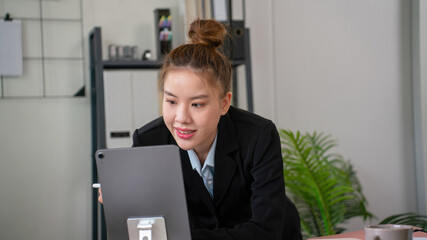 Businesswoman sitting at desk on couch in workplace or at home working on laptop and analyzing data on charts and graphs and writing on papers to make business plan and strategies for company.