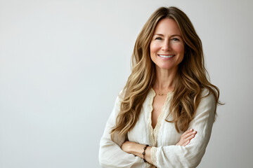 Fototapeta premium Confident Woman Portrait: A middle-aged woman with long, wavy brown hair smiles confidently with her arms crossed, exuding strength and self-assurance. 