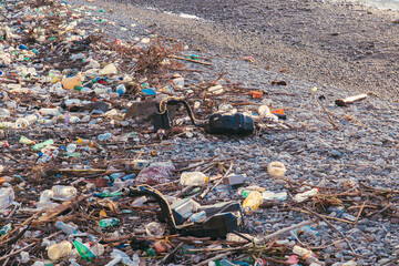 Polluted beach covered with plastic waste, bottles, and debris washed ashore. Ocean waves in the background during sunset. Highlights environmental pollution and ecological issues.
