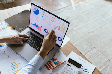 Business professional in modern office analyzing financial charts on laptop. Corporate strategy,...