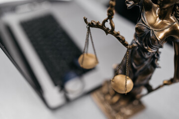 Close-up of a lawyer's desk with a laptop, glasses, and a statue of Themis. A symbol of justice and...