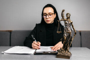 A lawyer is working at his desk, sorting papers. A statue of Themis stands nearby. The concept of...