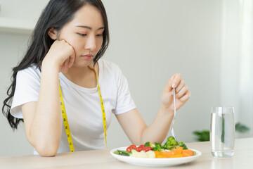 unhappy asian women is on dieting time looking at broccoli on the fork. girl do not want to eat vegetables and dislike taste of broccoli.