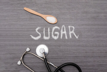 Granulated sugar forming the word sugar near a stethoscope and a wooden spoon lying on a gray...