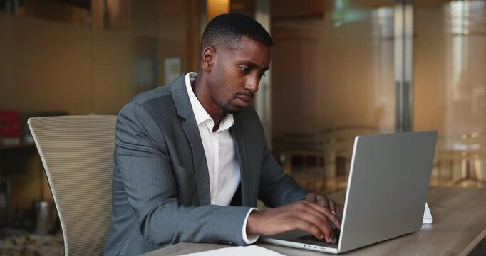 African man working in office using laptop, preparing report, review data or information, revising marketing plans or strategy looks focused and productive. Workflow, modern wireless technology usage
