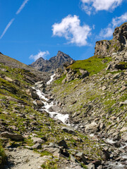 Alpines Hochgebirgstal mit Wasserfall in den Walliser Alpen bei blauem Himmel