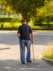 Älterer Mann mit Gehstock geht allein auf Gehweg bei Sonnenschein