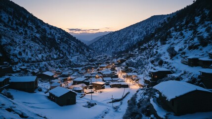 Snow-covered village in a valley during twilight with warm lights glowing from cabins